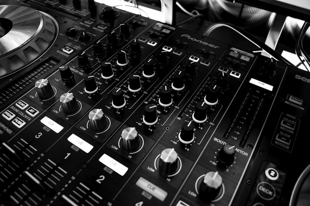 Black and white close-up of a DJ's audio mixing console with knobs and controls.